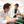 Two La Sierra students in lab coats are engaged in a discussion while working in a laboratory. One is leaning over a table, while the other holds lab equipment. The setting includes various scientific instruments and lab supplies