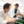 Two La Sierra students in lab coats are engaged in a discussion while working in a laboratory. One is leaning over a table, while the other holds lab equipment. The setting includes various scientific instruments and lab supplies